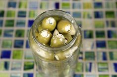 a glass jar filled with green olives sitting on top of a tiled countertop