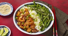 a bowl filled with shrimp, rice and green beans next to chopsticks on a red table