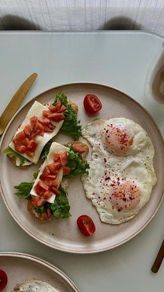 two plates with eggs, tomatoes and lettuce on them next to silverware