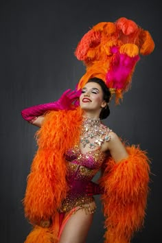 a woman in an orange and pink costume with feathers on her head, posing for the camera