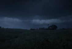 a dark sky with some clouds in the distance and grass on the ground below it