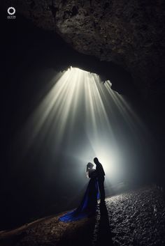 a man and woman standing in front of a cave with light coming from the ceiling