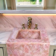 a marble sink with gold faucets in front of a window