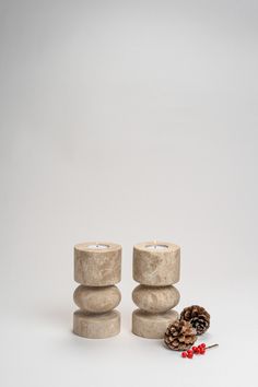 two candles sitting next to each other near pine cones