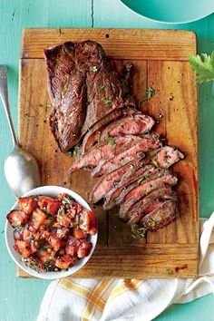 sliced steaks and vegetables on a cutting board next to a bowl of sauce with spoon