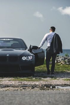 a man standing next to a black car near the ocean