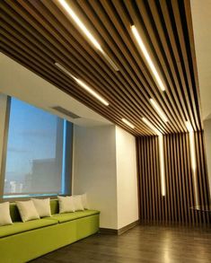 a green couch sitting in front of a window next to a wooden ceiling with lights