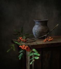 a vase sitting on top of a wooden table next to a branch filled with berries