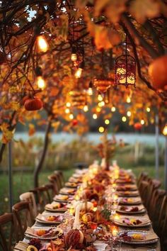 an outdoor dinner table set up with fall leaves and pumpkins on the table, surrounded by hanging lights