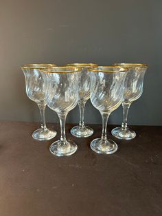 four clear wine glasses with gold rims on a brown table top next to a gray wall