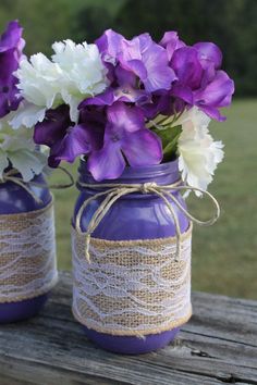 two mason jars with purple and white flowers in them sitting on a wooden table outside