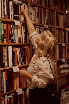 a woman is reaching up to reach books on a book shelf in front of a wall full of books