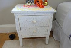 a white nightstand with two decorative items on top and a night stand next to it