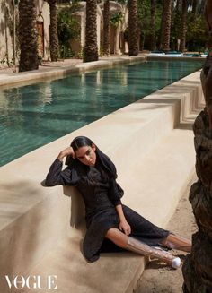 a woman sitting on the edge of a swimming pool next to palm trees and water