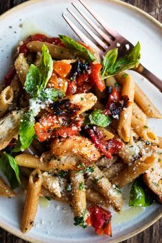 a white plate topped with pasta covered in sauce and veggies next to a fork