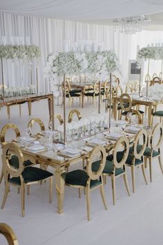 a table set up for a formal dinner with gold chairs and white flowers on the tables