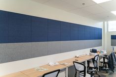 an empty office with desks and chairs in front of a large blue paneled wall