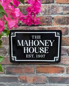 the mahoney house sign is next to pink flowers on a brick wall in front of it