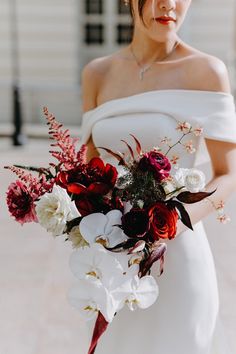 a woman in a white dress holding a red and white bouquet