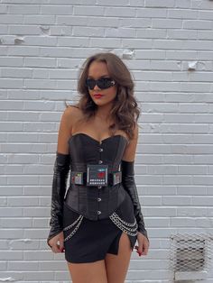 a woman in a black corset and sunglasses poses for the camera with her hands on her hips