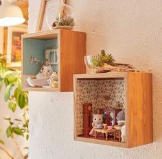 two wooden boxes with miniature houses in them hanging on the wall next to a potted plant