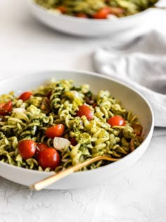 two bowls filled with pasta and vegetables on top of a white tablecloth next to gold spoons