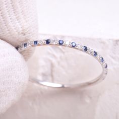 a white gold ring with blue sapphires and diamonds on the side, resting on a pillow