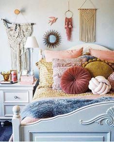 a white bed topped with lots of pillows next to a wall mounted mirror and lamp