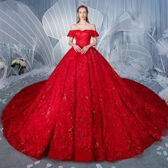 a woman in a red ball gown standing next to a white fairy wings backdrop with flowers