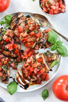 grilled chicken with tomatoes and basil garnishes on a white platter