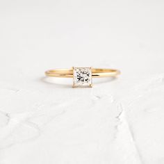 a yellow gold engagement ring with a princess cut diamond in the center on a white background