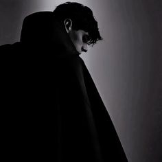 a man in a black cloak with his face covered by a hoodie looking down