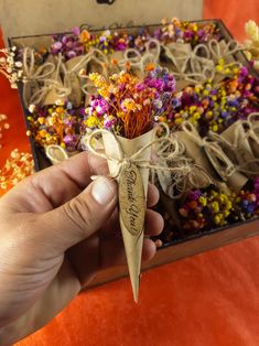 someone is holding a small bouquet of flowers in front of an orange table cloth covered box