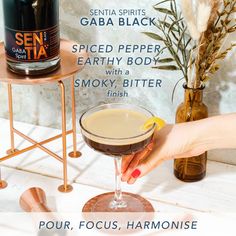 a woman is holding a drink in her hand with the caption pour focus, harmonise gaba black spiced pepper earthy body smoky bitter finish