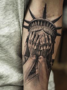 a person with a tattoo on their arm holding the statue of liberty's hands