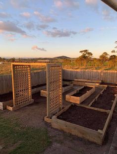 an outdoor garden area with raised beds and trelliss on the ground, in front of a wooden fence