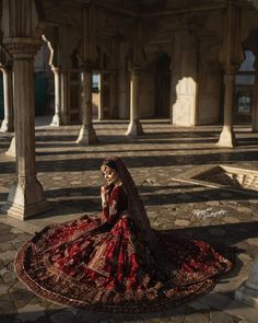 a woman in a red and gold wedding dress sitting on a stone floor next to pillars