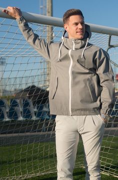 a man standing in front of a soccer goal wearing a gray jacket and white pants