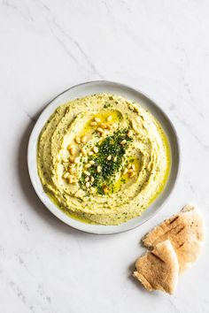 hummus and pita chips on a white plate with pesto sauce in the middle