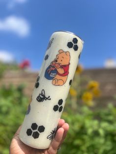 a hand holding a glass with winnie the pooh on it and bees around it