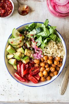 a bowl filled with vegetables and grains next to some silverware on a white table