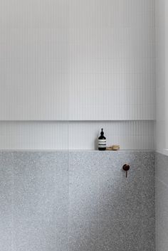 a white tiled bathroom with a shower head and soap dispenser on the wall