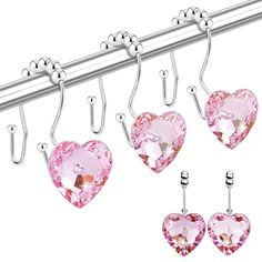 three heart shaped pink crystal earrings hanging from hooks on a metal bar with two clips