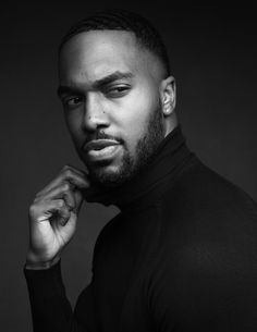 a black and white photo of a man with his hand on his chin looking at the camera