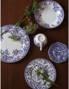 blue and white plates with flowers on them sitting on a wooden table next to a vase