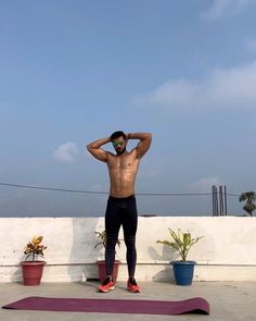 a shirtless man standing on top of a yoga mat with his hands behind his head