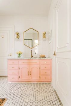 a bathroom with white walls and pink vanity, gold mirror, and hexagonal tile floor