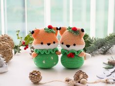 two crocheted stuffed animals sitting on top of a table next to pine cones