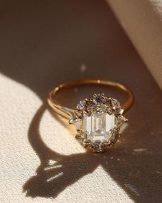 an engagement ring sitting on top of a white cloth covered floor next to a shadow from the sun