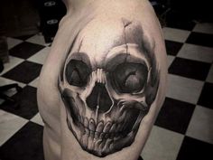 a man with a skull tattoo on his arm and shoulder is standing in front of a black and white checkered floor